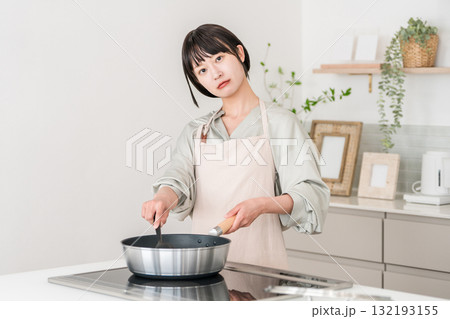 キッチンのIHコンロの前で考える,悩む迷いながら料理するエプロン姿の若いアジア人女性 キッチンのIHコンロの前で考える,悩む迷いながら料理するエプロン姿の若いアジア人女性 132193155
