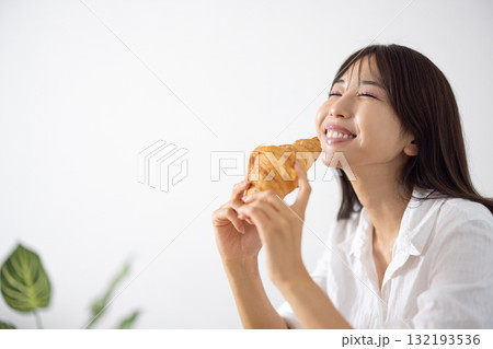 笑顔でクロワッサンを食べる若い女性 132193536