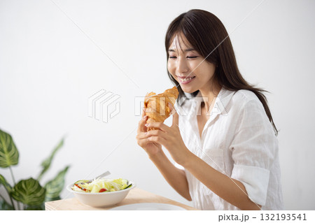 笑顔でクロワッサンを食べる若い女性 笑顔でクロワッサンを食べる若い女性 132193541
