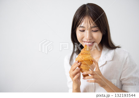 笑顔でクロワッサンを食べる若い女性 132193544