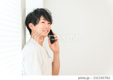 スマホで電話する若いアジア人男性（家,リビング,笑顔） 132193762