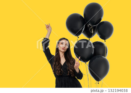 Young woman wearing a black dress poses with black balloons Young woman wearing a black dress poses with black balloons 132194038