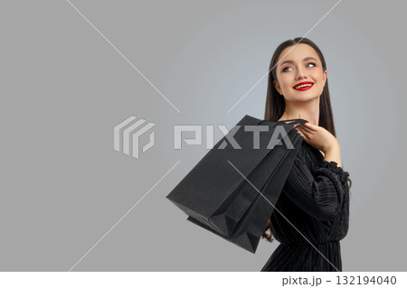 Woman wearing black dress holding shopping bags and smiling Woman wearing black dress holding shopping bags and smiling 132194040