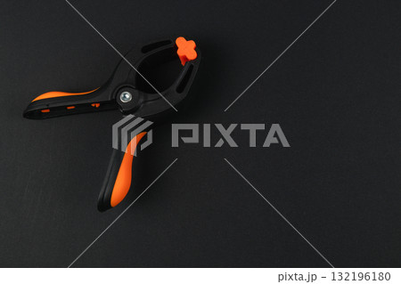 Black and orange clamp on dark surface with a smooth texture 132196180