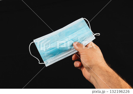 Hand holding a blue surgical mask against a black background Hand holding a blue surgical mask against a black background 132196226