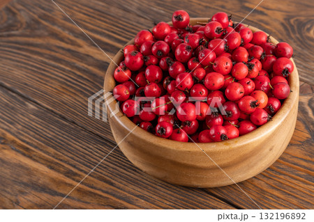 red hawthorn berries in wooden bowl on flat wooden surface 132196892