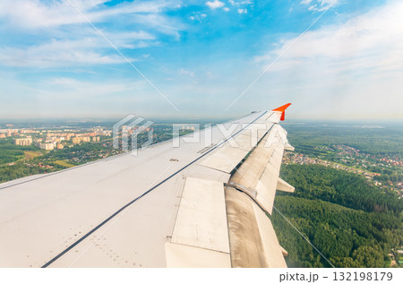 View of airplane wing, blue skies and green land during landing. Airplane window view. 132198179