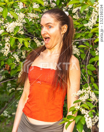 Young woman sneezes in the park against the background of a flowering tree. Allergy to pollen concept. 132198194