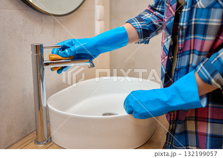 Woman cleaning bathroom faucet with sponge and gloves Woman cleaning bathroom faucet with sponge and gloves 132199057