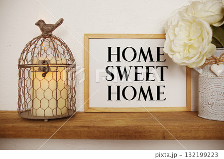 Home Sweet Home text written on whiteboard with LED candle light and bird cage on wooden shelf 132199223