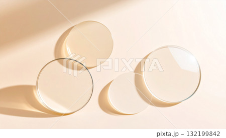 Top-down view of transparent glass discs on a soft beige background with shadows. 132199842