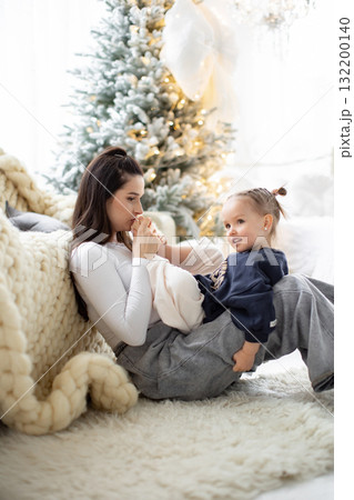 A tender moment between a mother and her daughter during the Christmas season, with a decorated tree in the background. 132200140