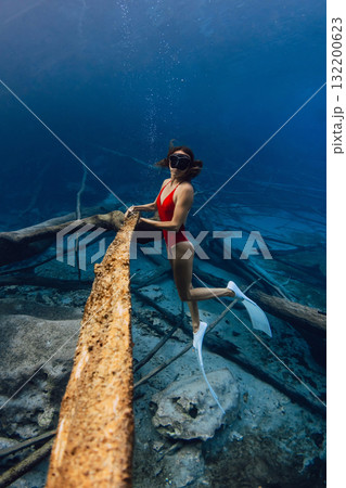 Woman freediver underwater holding sunken wooden log in the lake. Freediving in blue crystal lake Woman freediver underwater holding sunken wooden log in the lake. Freediving in blue crystal lake 132200623