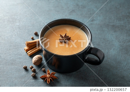 Traditional Indian masala chai tea with milk and spices in a black cup on a dark background close up 132200657