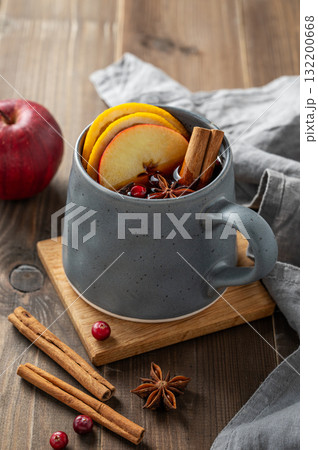 A cup of red mulled wine with spices, orange, apple slices and cranberry on a wooden background 132200668