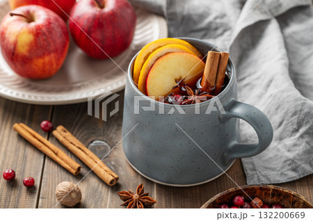 A cup of red mulled wine with spices, orange, apple slices and cranberry on a wooden background 132200669