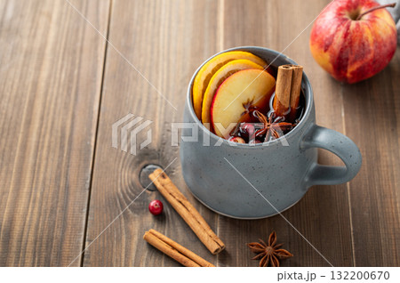 A cup of red mulled wine with spices, orange, apple slices and cranberry on a wooden background 132200670