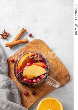 A cup of red mulled wine with spices, orange and apple slices on a wooden board on light background 132200695