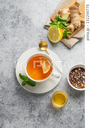 Tea with lemon, ginger, honey, and mint in a cup on a gray background with citrus fruits and herbs. Tea with lemon, ginger, honey, and mint in a cup on a gray background with citrus fruits and herbs. 132200778
