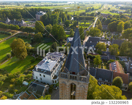 Aerial view of town with central Gothic style church, pointed steeple, red and gray rooftops, tree lined streets, and parked cars blending history with modern life. 132200965
