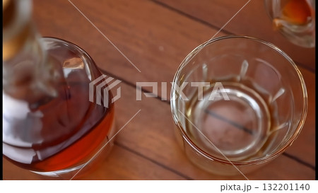 木目のテーブルに置かれた琥珀色の酒が入ったボトルと空のグラス 132201140