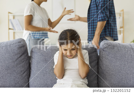 Sad child holding hands to ears to cover and ignore parents quarrel at home Sad child holding hands to ears to cover and ignore parents quarrel at home 132201152