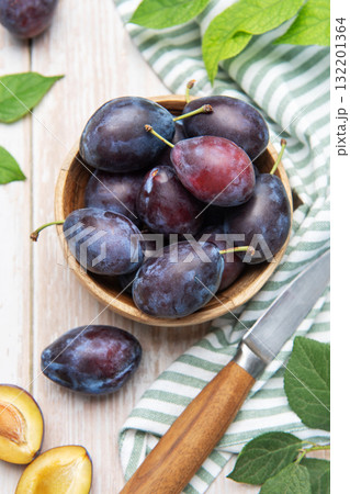 Fresh plums in wooden bowl with knife 132201364
