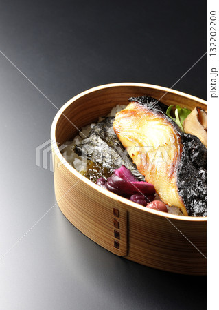曲げわっぱに入っていて銀鱈の西京焼が乗っている海苔弁当を黒背景で撮影 132202200