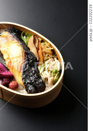 曲げわっぱに入っていて銀鱈の西京焼が乗っている海苔弁当を黒背景で撮影 132202219