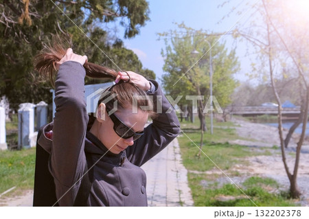 Portrait of woman makes ponytail walking in city park, she does her hairs. Portrait of woman makes ponytail walking in city park, she does her hairs. 132202378
