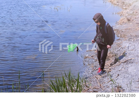 Boy is cathcing frogs and fish on the river using butterfly net. Boy is cathcing frogs and fish on the river using butterfly net. 132202380