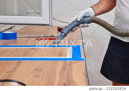 Worker man vacuums new kitchen after cutting hole for the sink in the kitchen countertops Worker man vacuums new kitchen after cutting hole for the sink in the kitchen countertops 132203814