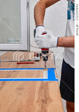 repairman using electric drill for cutting hole for the sink in the kitchen countertops, installation new modern kitchen 132203842