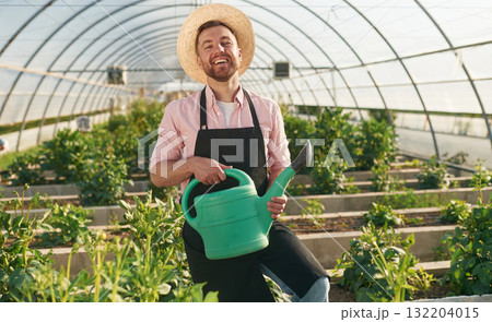 Watering can in hands. Man in greenhouse is working with plants Watering can in hands. Man in greenhouse is working with plants 132204015