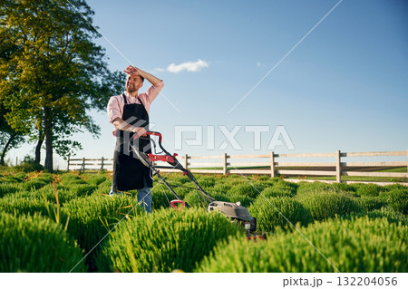 Handles the lawn mower. Adult farmer is outdoors Handles the lawn mower. Adult farmer is outdoors 132204056