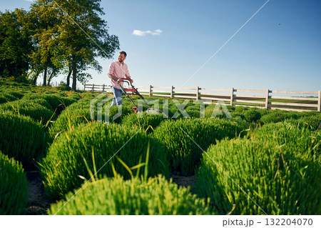 Fuel powered lawn mower. Adult farmer is outdoors Fuel powered lawn mower. Adult farmer is outdoors 132204070