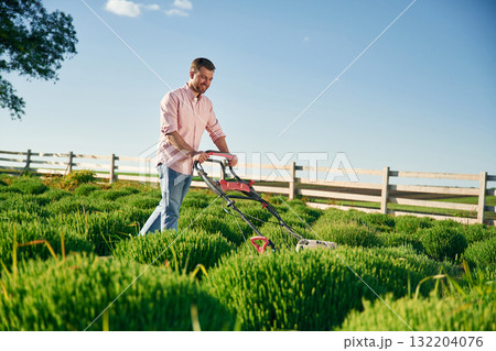 Red colored lawn mower. Adult farmer is outdoors Red colored lawn mower. Adult farmer is outdoors 132204076