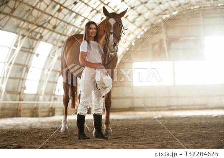 Daylight comes through the windows. Beautiful young woman is with horse indoors Daylight comes through the windows. Beautiful young woman is with horse indoors 132204625