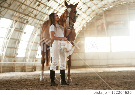 Daylight comes through the windows. Beautiful young woman is with horse indoors 132204626