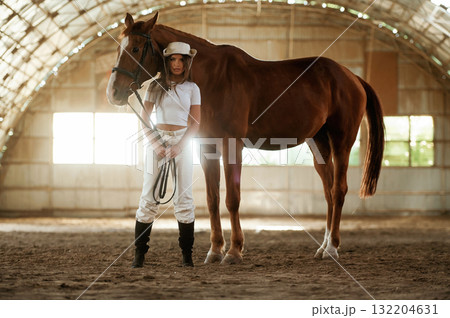 In the cowboy hat. Beautiful young woman is with horse indoors In the cowboy hat. Beautiful young woman is with horse indoors 132204631