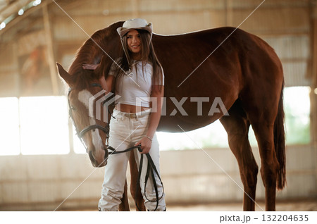 In the cowboy hat. Beautiful young woman is with horse indoors In the cowboy hat. Beautiful young woman is with horse indoors 132204635