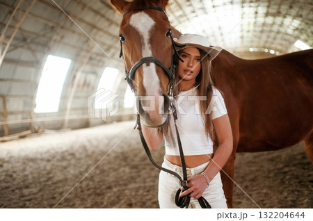 Looking forward. Beautiful young woman is with horse indoors Looking forward. Beautiful young woman is with horse indoors 132204644