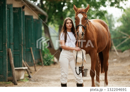 Animal stall on the side. Young beautiful woman is with a horse outdoors Animal stall on the side. Young beautiful woman is with a horse outdoors 132204691