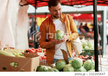 Choosing cabbage. Handsome man is on the street market or bazaar Choosing cabbage. Handsome man is on the street market or bazaar 132205647