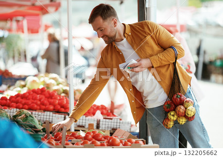 With a shopping list. Vegetables and fruits. Handsome man is on the street market or bazaar With a shopping list. Vegetables and fruits. Handsome man is on the street market or bazaar 132205662