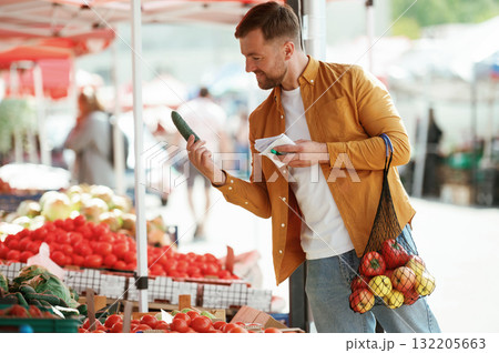 With a shopping list. Vegetables and fruits. Handsome man is on the street market or bazaar With a shopping list. Vegetables and fruits. Handsome man is on the street market or bazaar 132205663
