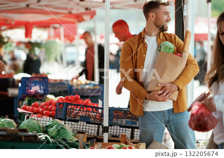 Shopping bag full of products. Handsome man is on the street market or bazaar Shopping bag full of products. Handsome man is on the street market or bazaar 132205674