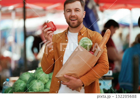 Baguette, pepper and cabbage in bag. Handsome man is on the street market or bazaar Baguette, pepper and cabbage in bag. Handsome man is on the street market or bazaar 132205688