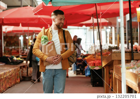 Smiling, holding shopping paper bag with products. Handsome man is on the street market or bazaar 132205701