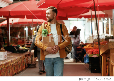 Smiling, holding shopping paper bag with products. Handsome man is on the street market or bazaar Smiling, holding shopping paper bag with products. Handsome man is on the street market or bazaar 132205702